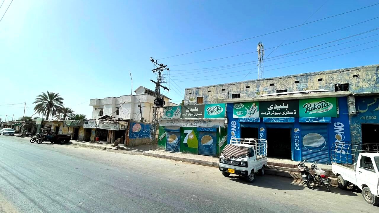The Buleedi Distributors shop front on the main road in Turbat: two adjoining units under Pakola and Pepsi boards, both signed in Urdu, with a delivery loader parked outside.